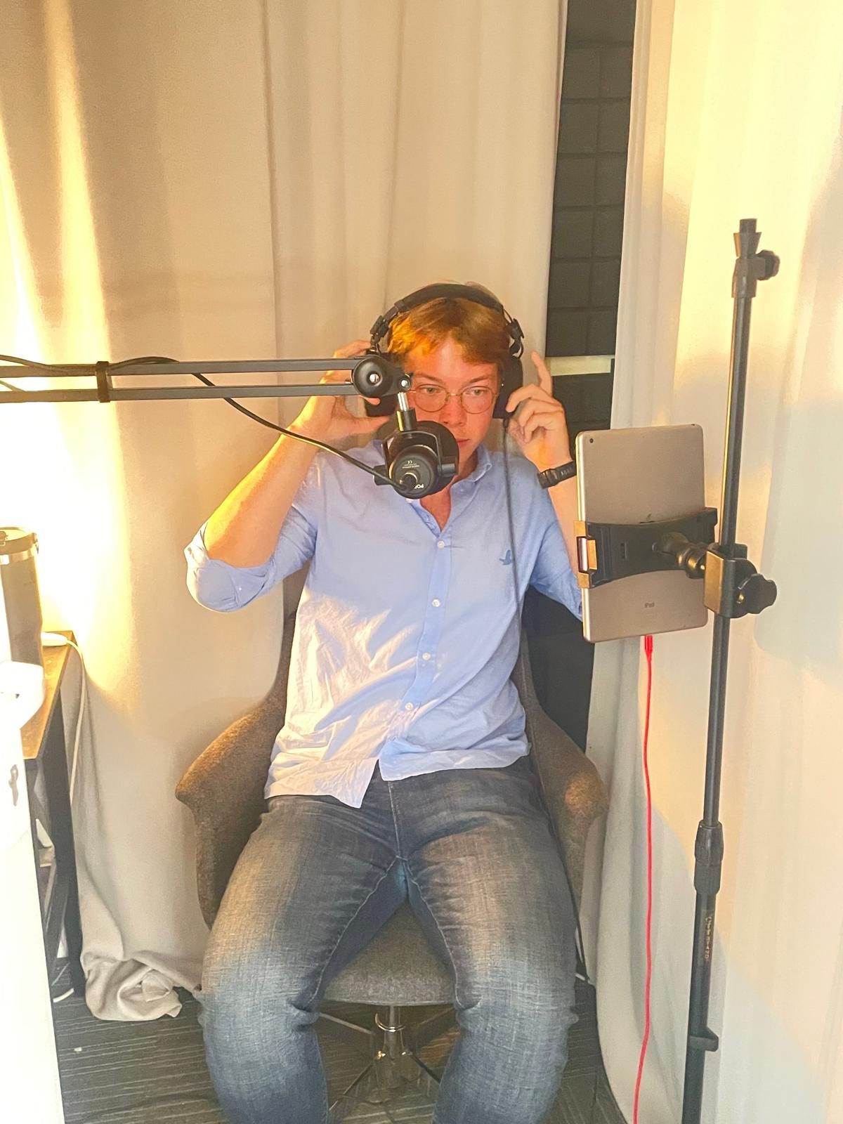 Recording the Turkish audiobook in a studio booth, headphones on, script on a tablet