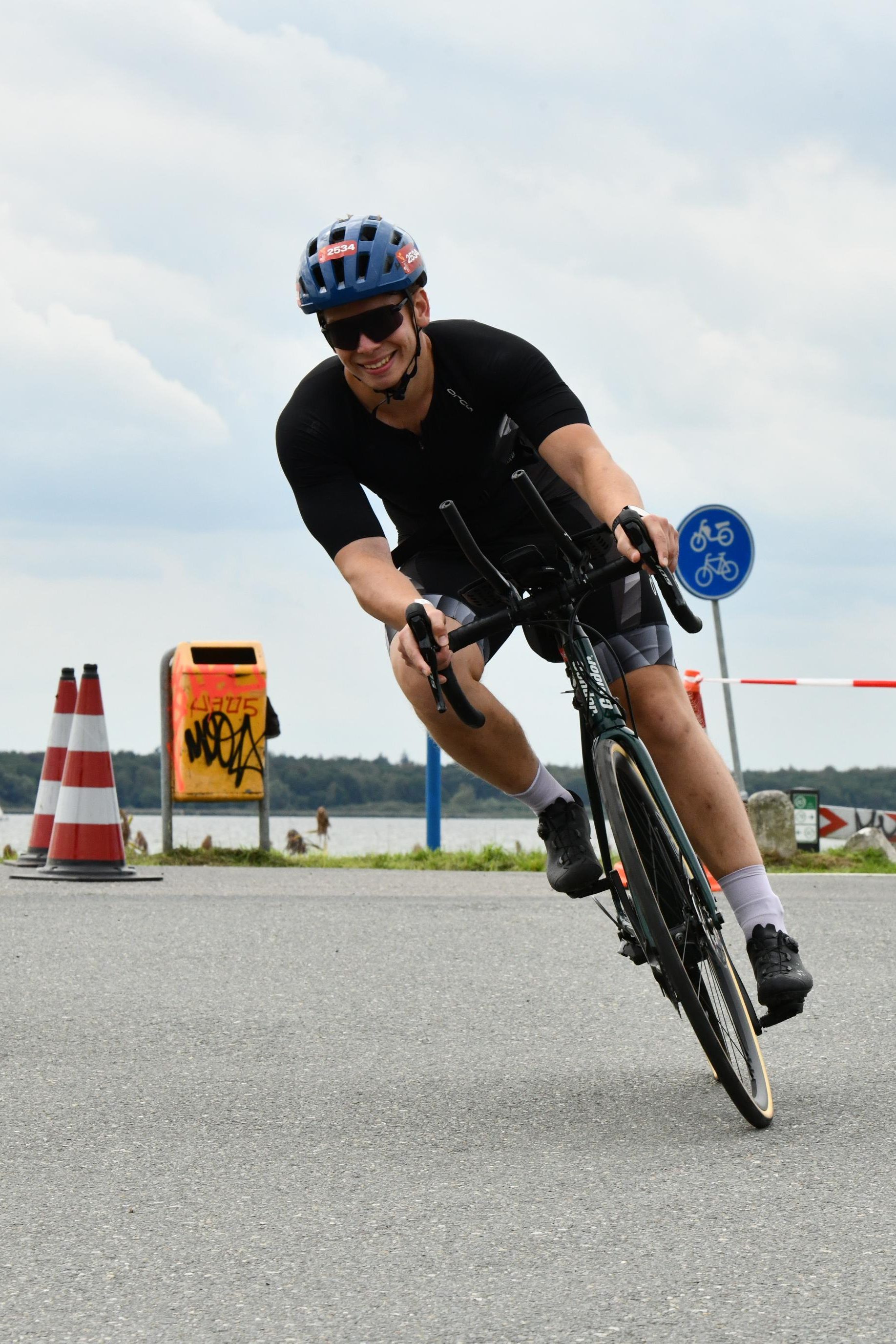 Leaning a road bike through a corner beside the water, race number 2534 on the helmet